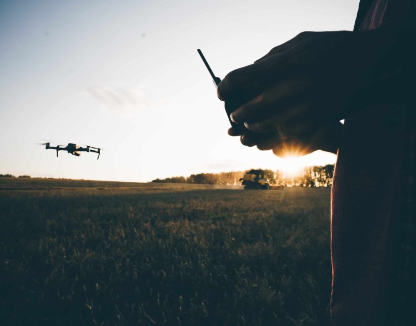 Drone for industrial works flying above combine harvester. Farmer navigating drone above farmland with combine at the background. High technology innovations in agriculture.